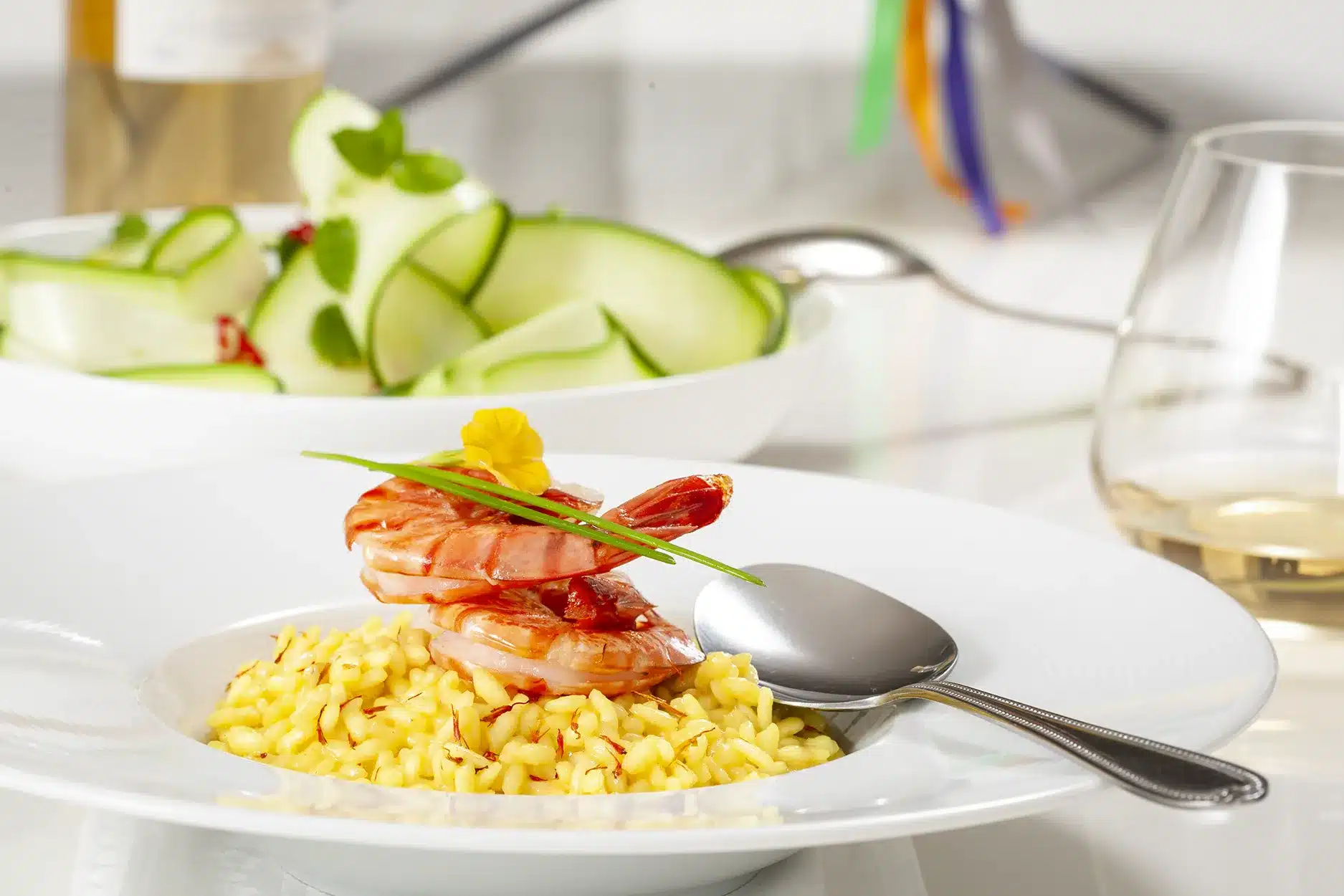 Lepel die door romige saffraanrisotto met gamba’s gaat, geserveerd op een wit bord.