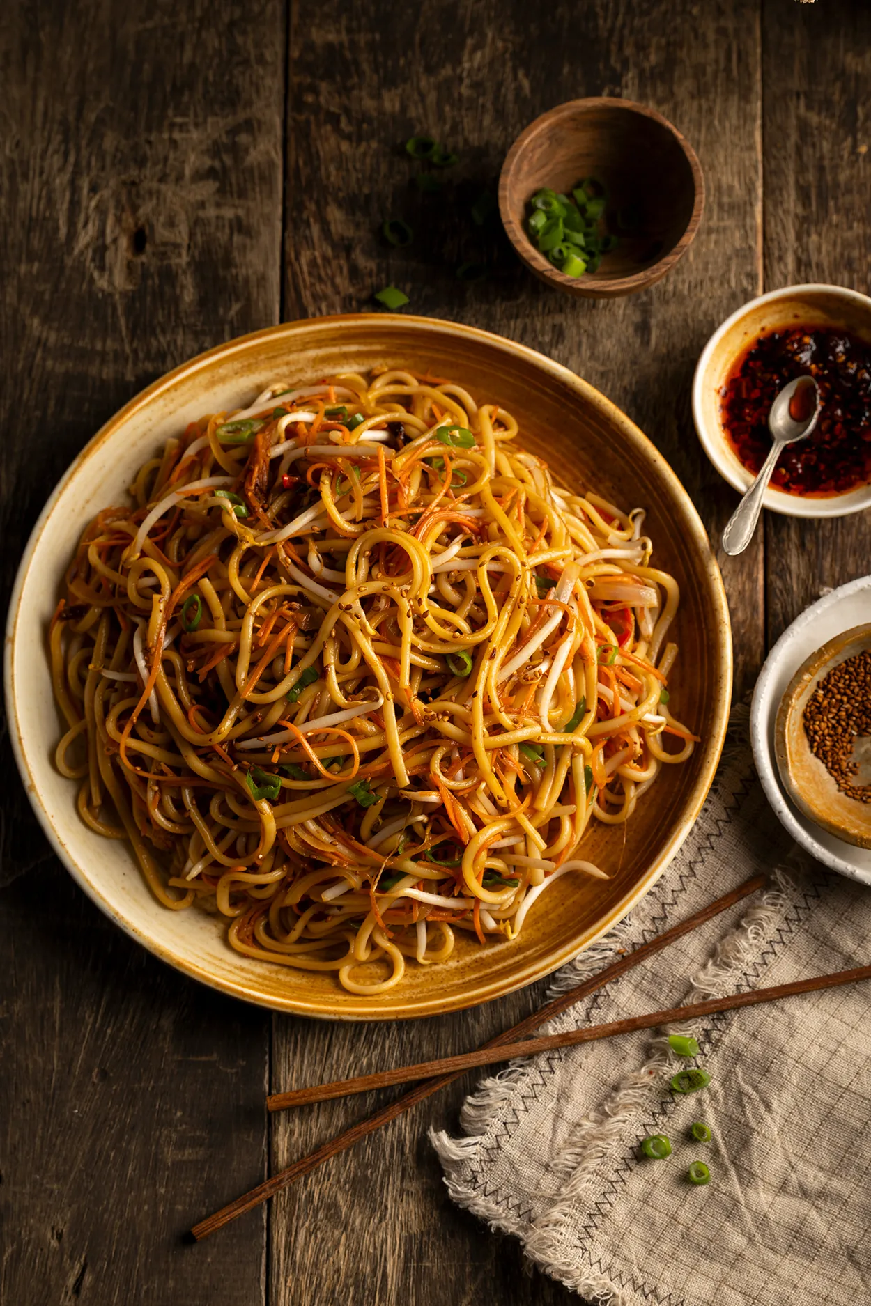 Chow Mein noedels met taugé, wortel en lente-ui in keramieken schaal, geserveerd met stokjes en chili-olie.
