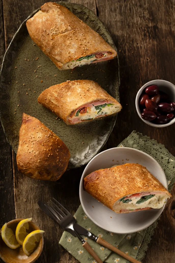 Goudbruine stromboli met spinazie, ricotta en Italiaanse vleeswaren op rustieke schaal met olijven