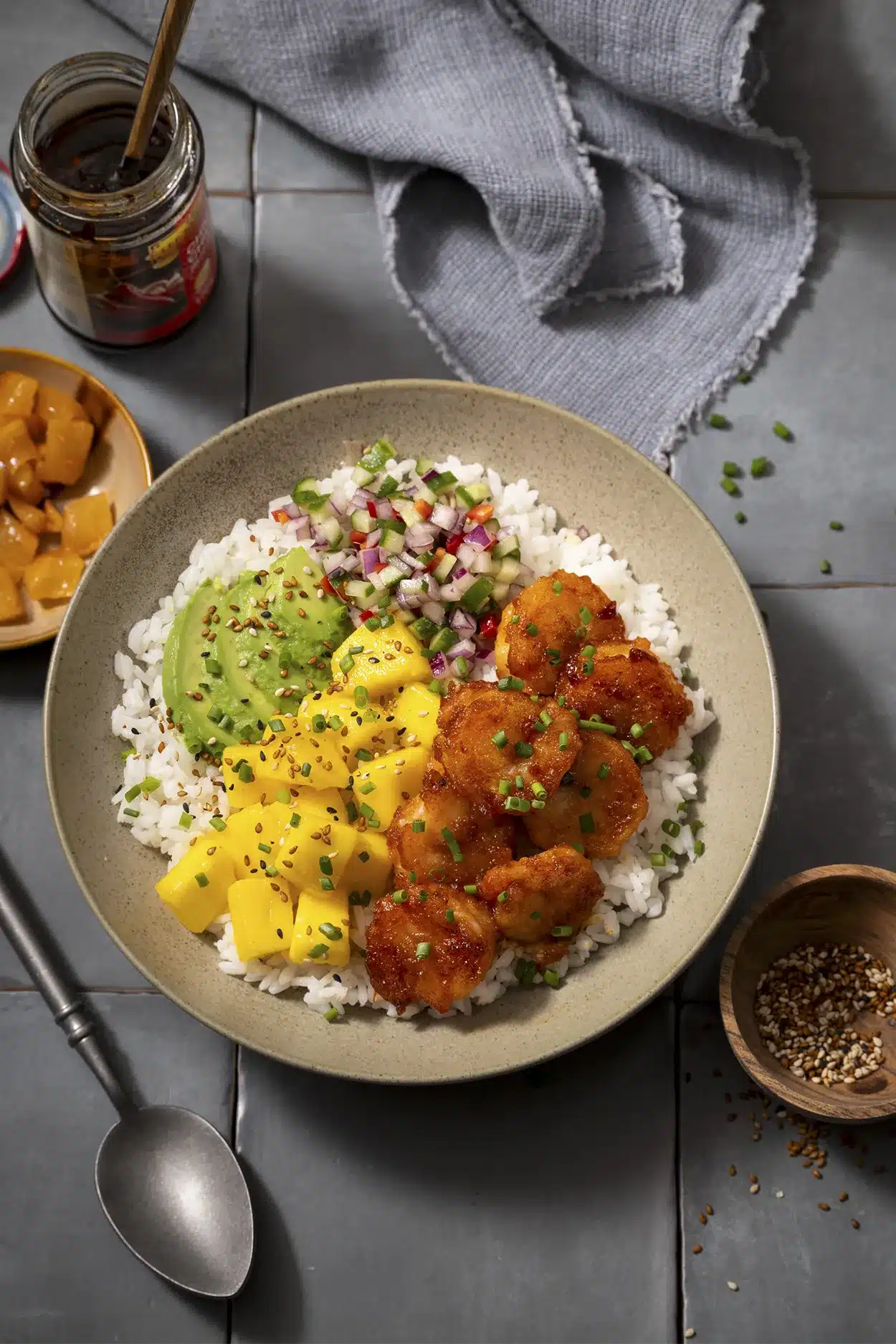 Poké bowl met garnalen en mango geserveerd met chili olie en sesam